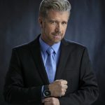 A photo of the mentalist Banachek wearing a dark suit with a light blue shirt and light blue tie