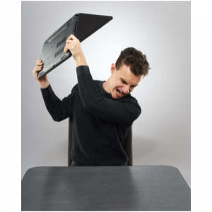 A photo of a man angrily smashing his laptop on a desk.