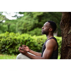 A picture of a man sat in nature meditating.