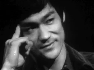 A black and white photo of Bruce Lee tapping his temple with his finger.