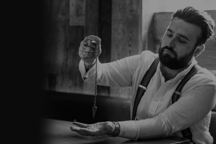 A black and white photo of Luke Jermay holding a pendulum