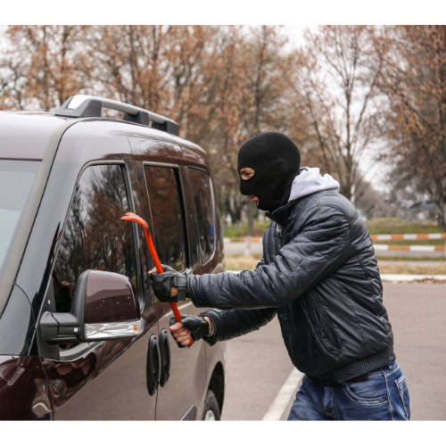 Man wearing a balaclava breaking into a car with a crowbar